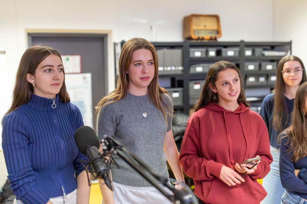 Gruppe von jungen Frauen steht in einem Raum mit gelbem Boden vor einem Fenster