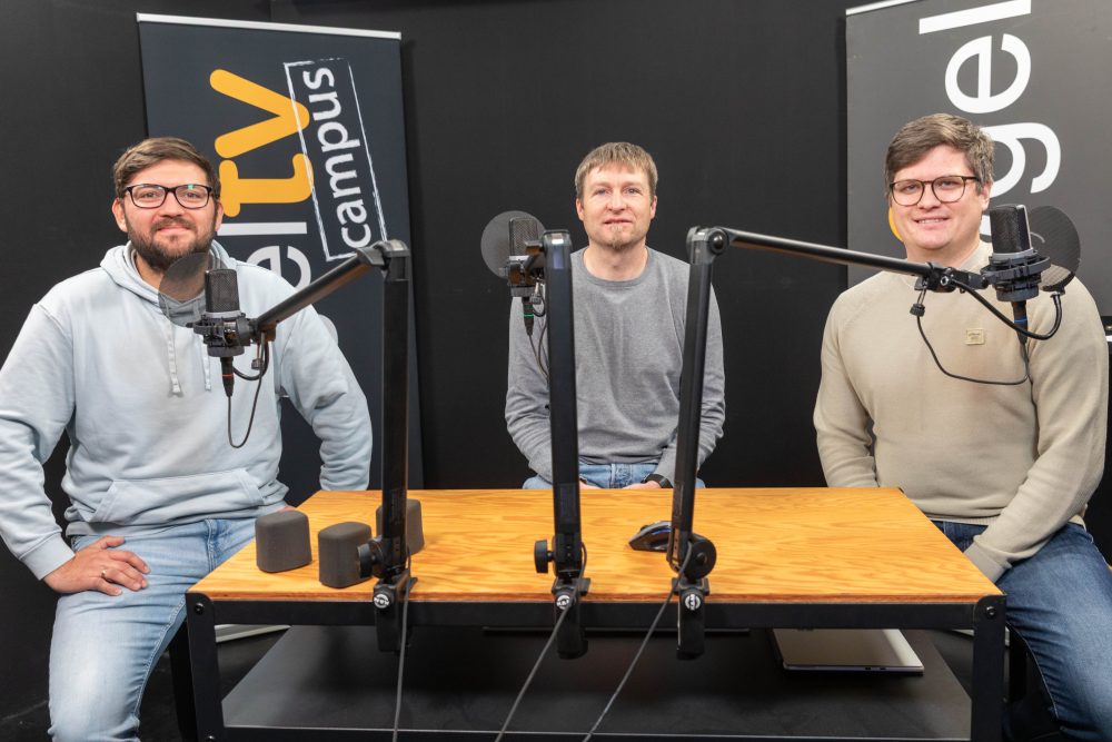 drei Herren in einem Tonstudio vor Mikrofonen, sitzend