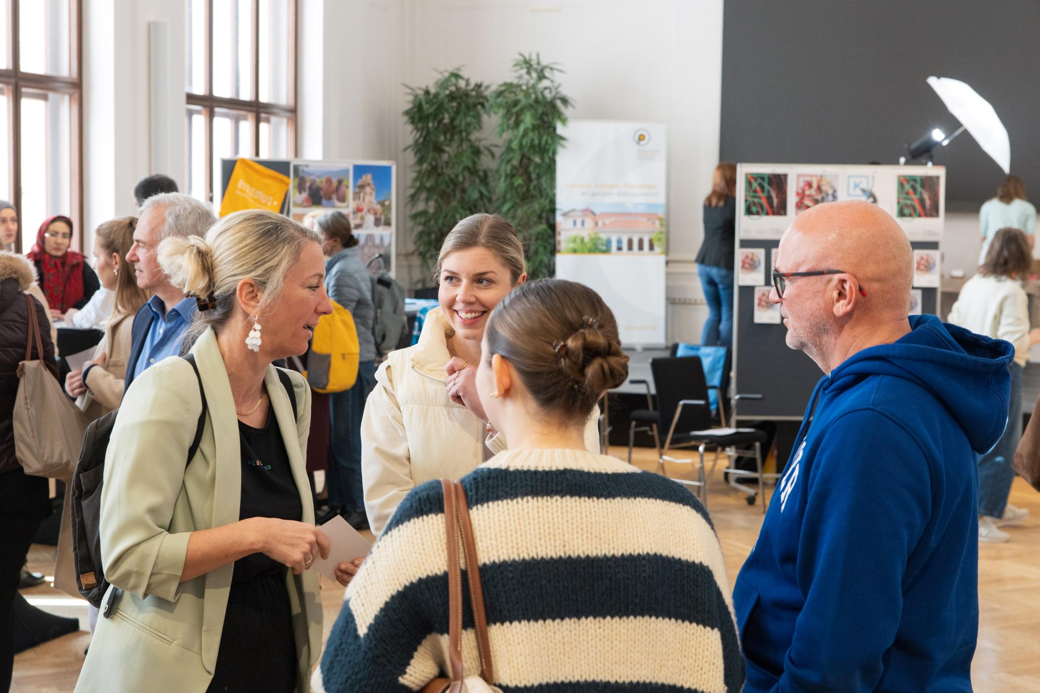 Vier Menschen im Gespräch im Vordergrund. Im Hindergrund Menschen an Infoständen.